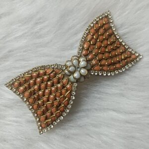 Gold-tone orange Kundan bow hair clip with floral center accent on soft background