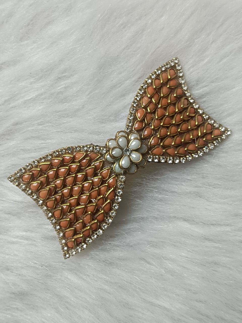 Orange Kundan Bow Design Gold-Tone Barrette Hair Clip Gold-tone orange Kundan bow hair clip with floral center accent on soft background