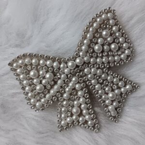 Silver-tone pearl bow hair clip with crystal accents on a soft textured background