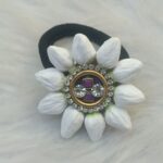 Close-up of black elastic scrunchie with white edelweiss-style flower petals and gold jeweled center featuring purple crystal and rhinestones