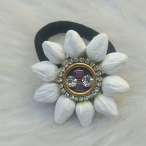 Close-up of black elastic scrunchie with white edelweiss-style flower petals and gold jeweled center featuring purple crystal and rhinestones